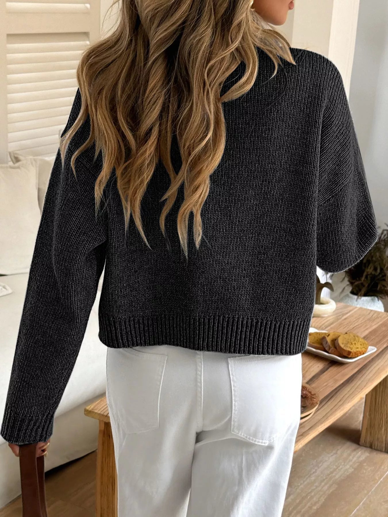 Person wearing a dark grey sweater and white pants in a casual setting.