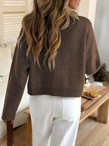 Person wearing a brown sweater and white pants in a home setting