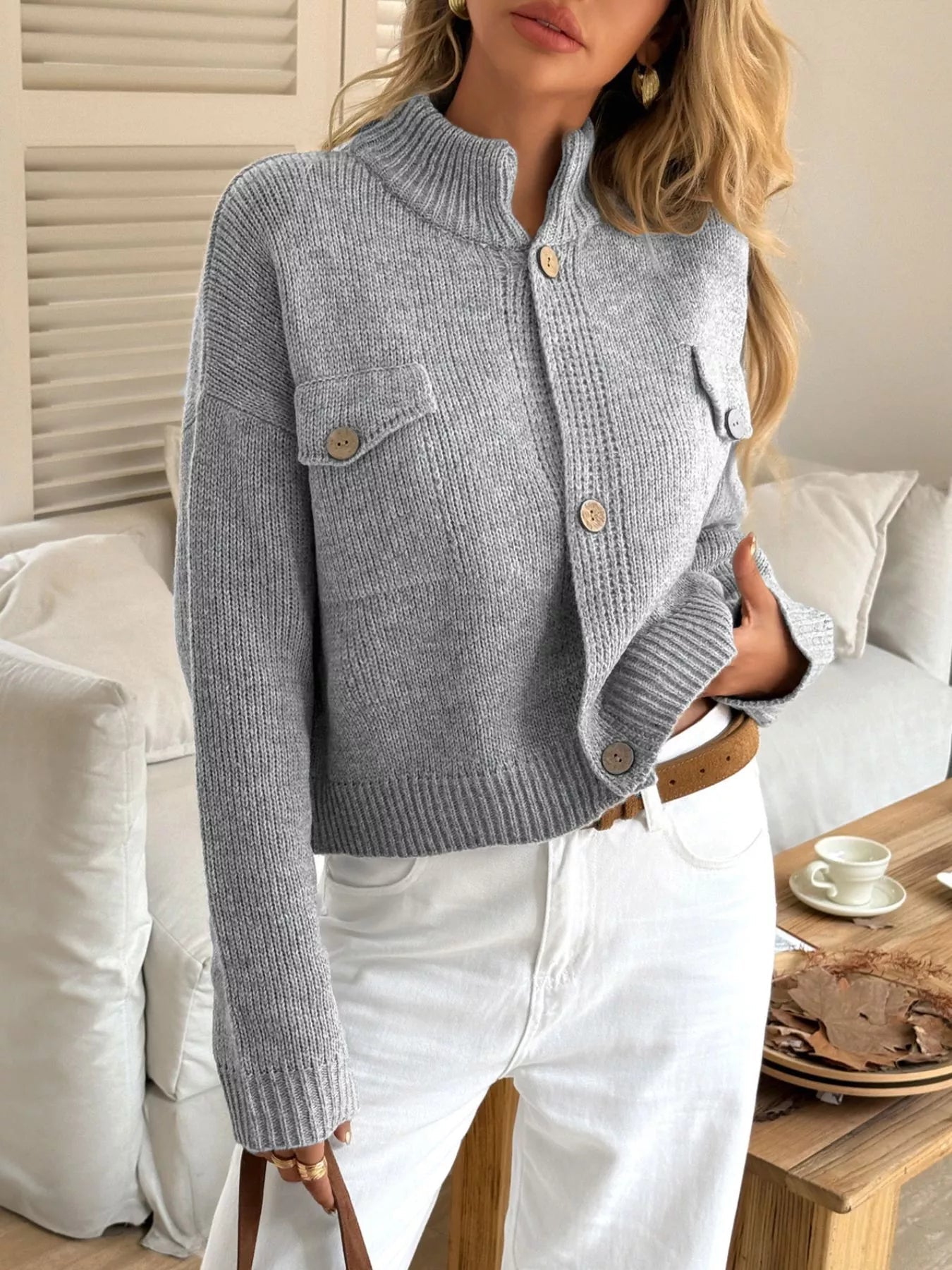 Woman wearing a light blue knitted cardigan with button details in a cozy living room setting.