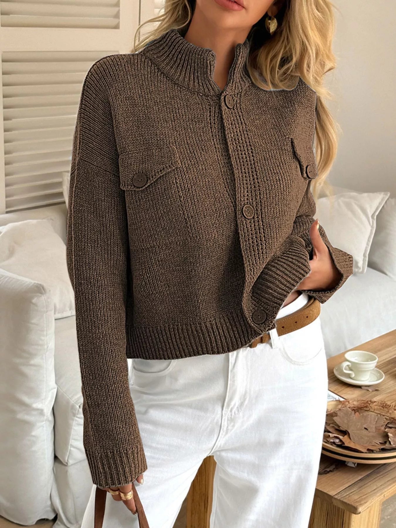 Woman wearing a brown knitted cardigan in a cozy living room setting.