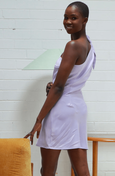 Woman wearing a light purple dress against a white brick wall.