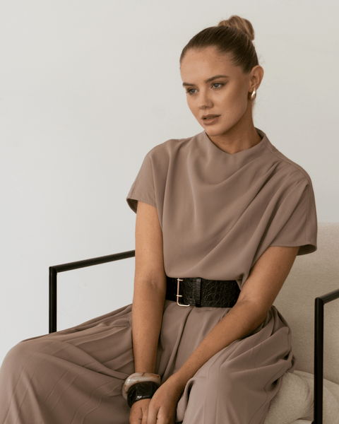 Model wears Sharee Top in taupe, seated with soft drape and cap sleeves visible.