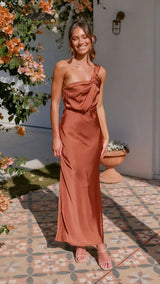 Woman in a rust-colored dress standing outdoors with flowers and a wall in the background