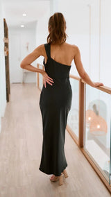 Woman in a black one-shoulder dress standing in a modern indoor setting.