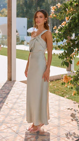 Woman in a light green dress standing outdoors with greenery and a pool in the background