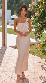 Woman in a beige strapless dress standing outdoors with greenery and flowers in the background