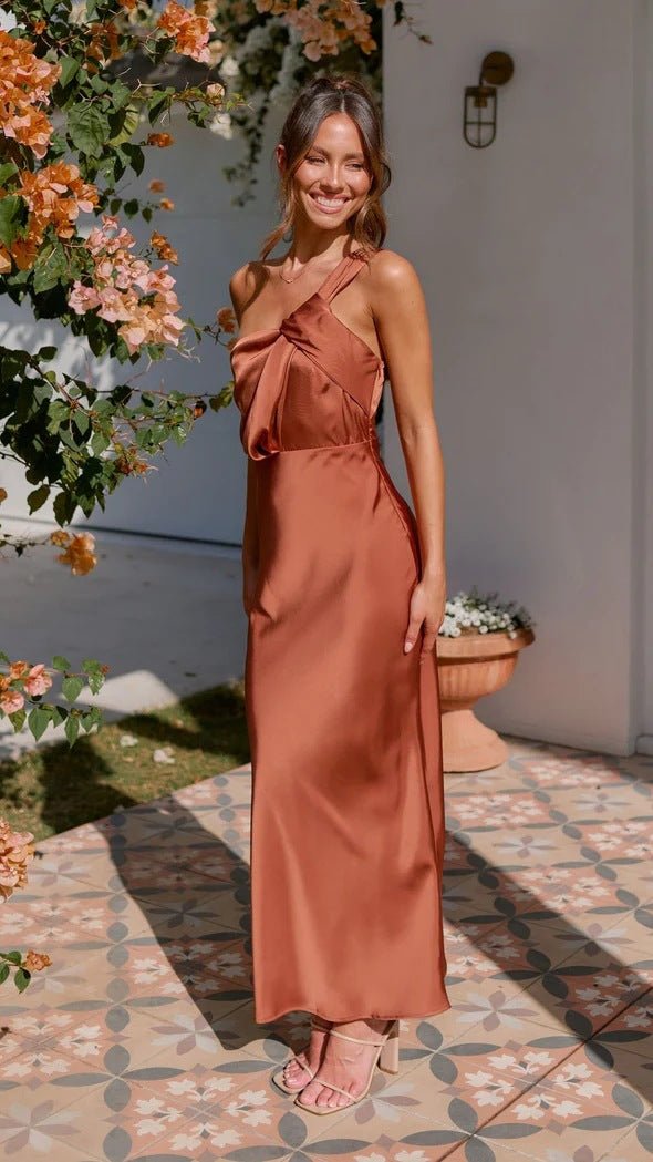 Woman in a rust-colored dress standing outdoors with flowers and a wall in the background