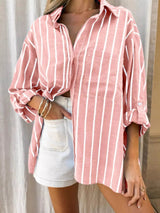 Person wearing a pink and white striped shirt with rolled-up sleeves and white shorts.