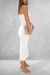 Woman in a white outfit holding a beige clutch against a gray background