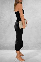 Woman wearing a black strapless top and satin skirt holding a beige clutch against a gray background