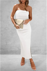 Woman wearing a white strapless dress holding a beige clutch against a gray background