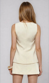 Woman wearing a light-colored sleeveless top and skirt set against a plain background