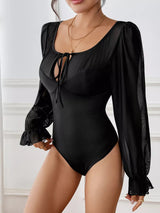 Black one-piece swimsuit with long sleeves on a neutral background