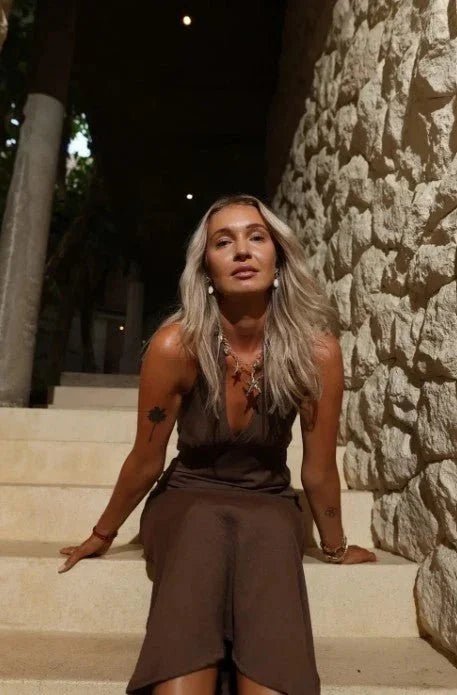 Woman in a brown halter neck maxi dress sitting on stone steps at night.