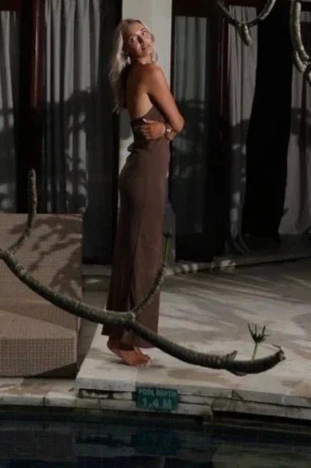 Woman in a brown halter neck maxi dress standing on a platform with a snake coiled around her
