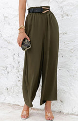 Woman wearing olive green wide-leg pants with a white textured wall background