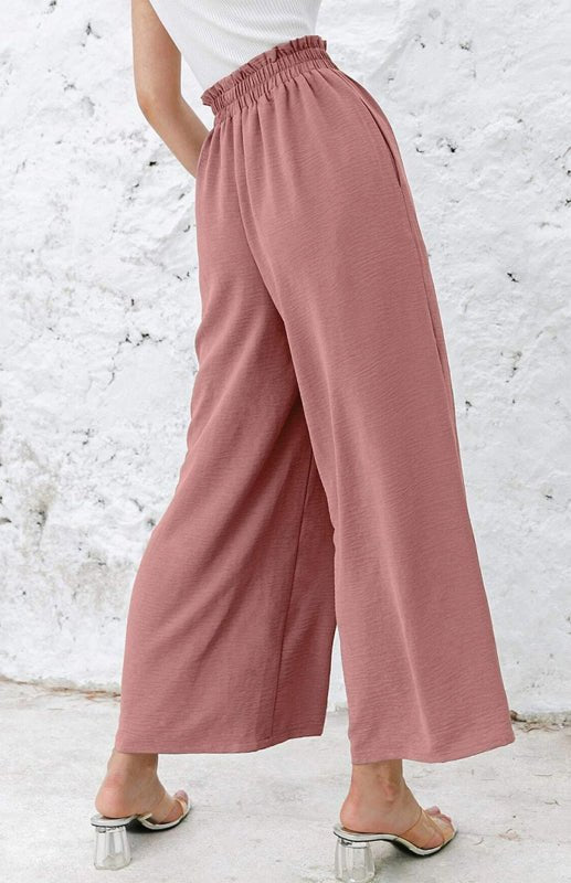 Woman wearing pink wide-leg pants against a white brick wall.