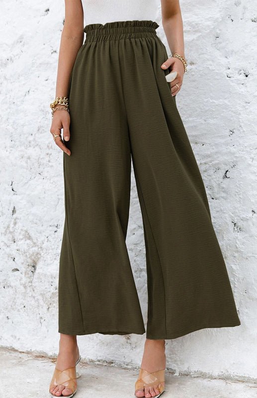 Woman wearing olive green wide-leg pants against a white textured wall.