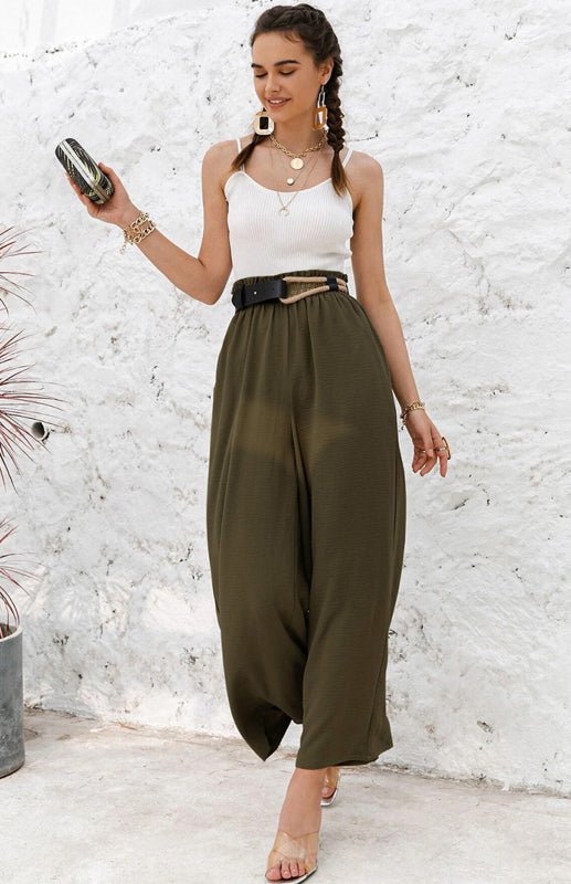 Woman wearing a white sleeveless top and olive green wide-leg pants against a textured white wall.