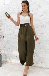 Woman wearing a white sleeveless top and olive green wide-leg pants against a textured white wall.