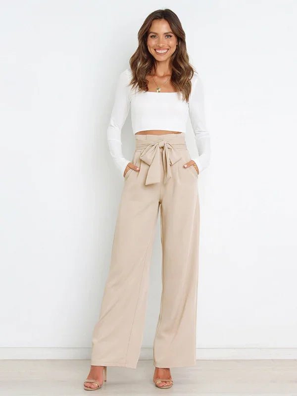 Woman wearing a white top and beige high-waisted pants with a belt against a white background
