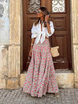 Model wears soft pink floral boho maxi skirt with white tied blouse and straw bag, styled for a romantic street look.