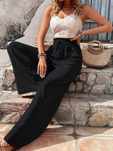 Woman in a white lace top and black high-waisted pants sitting on stone steps.