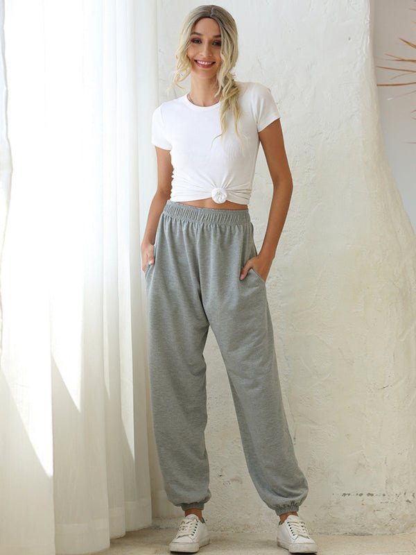 Woman wearing a white t-shirt and gray sweatpants standing against a white curtain.