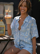 Woman wearing the Suvi two piece set in blue and white while sitting outdoors with iced coffee.