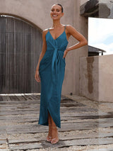 Woman in a teal dress standing on a wooden deck with a neutral background