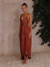 Woman in a rust-colored dress standing against a textured wall with greenery.