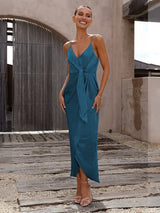 Woman wearing a teal dress standing on a wooden deck with a neutral background