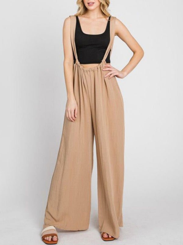 Beige Etana Overall Jumpsuit in studio setting, styled with a black tank top and heels.