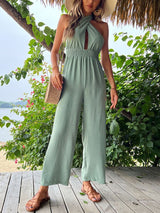Front walking view of The Sage Jumpsuit in soft green, styled with sandals and loose waves.